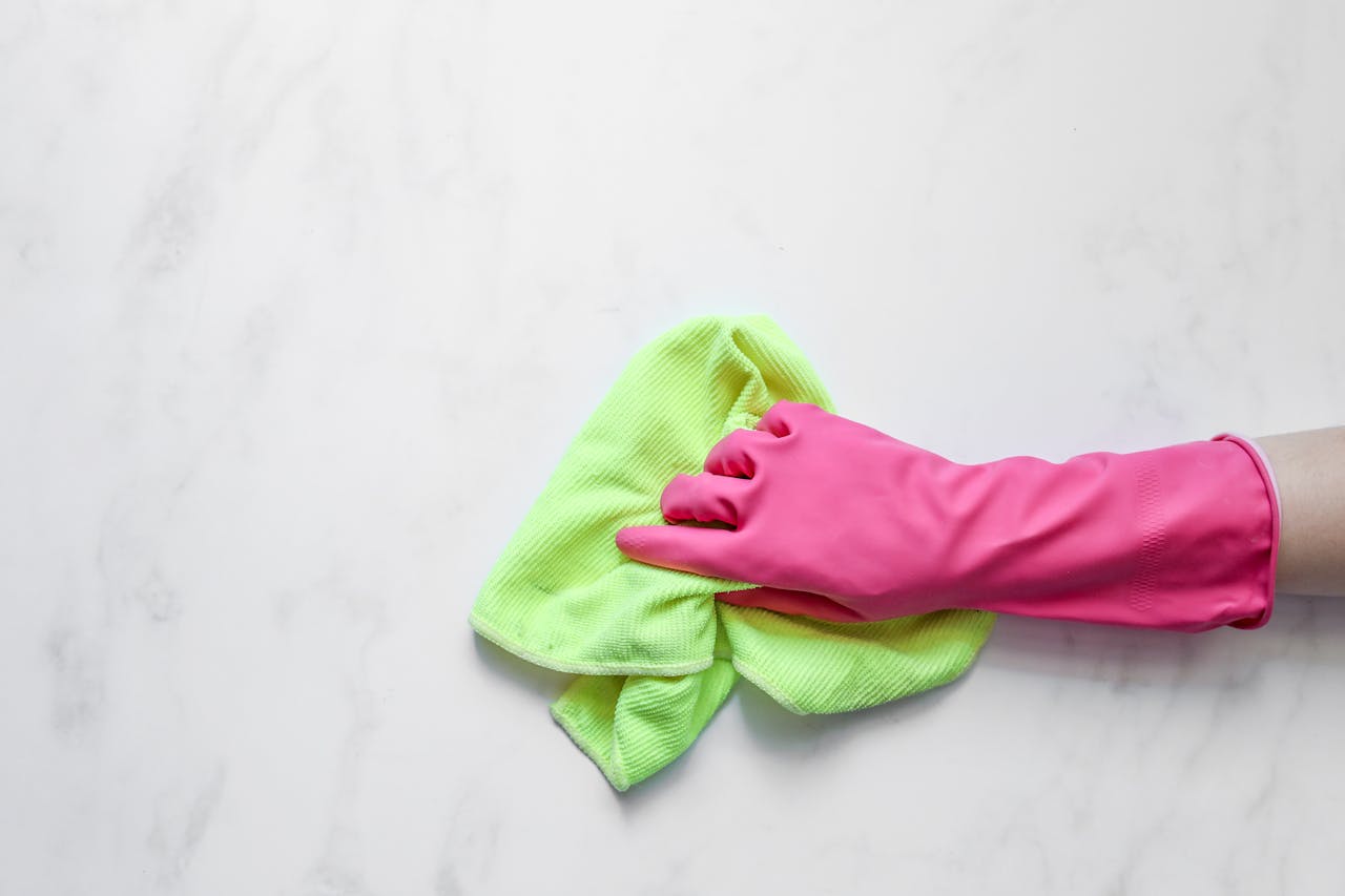our-story Pink rubber glove cleaning a surface with a green cloth on a white background.